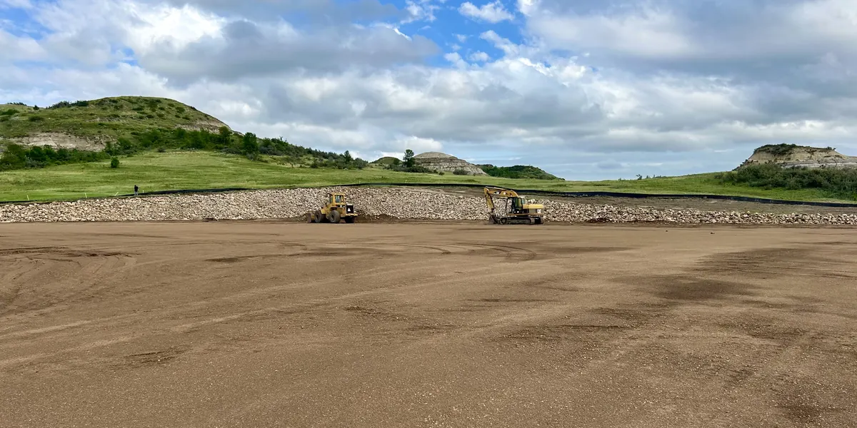 An Arkon Earth Construction loader and excavator working a gravel pad with buttes behind it