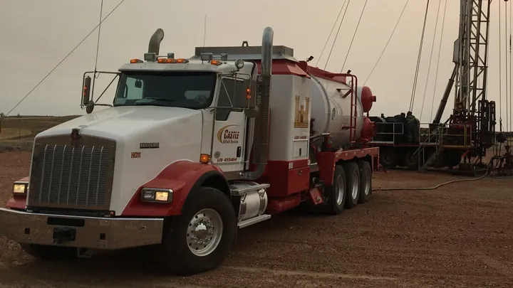 A Castle hot oil truck on location beside a workover rig