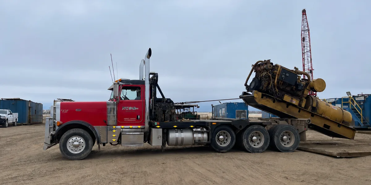 A red North Country Construction & Rentals Peterbilt winch truck pulling an engine skid up onto its bed