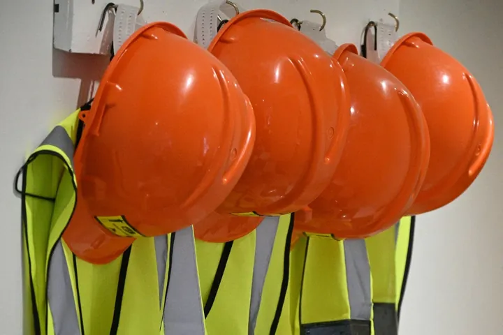 Orange hard hats and hi-vis vests hanging on a rack