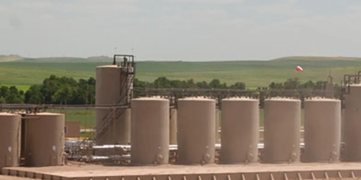 A tank facility with a stair tower and a windsock, green hills behind