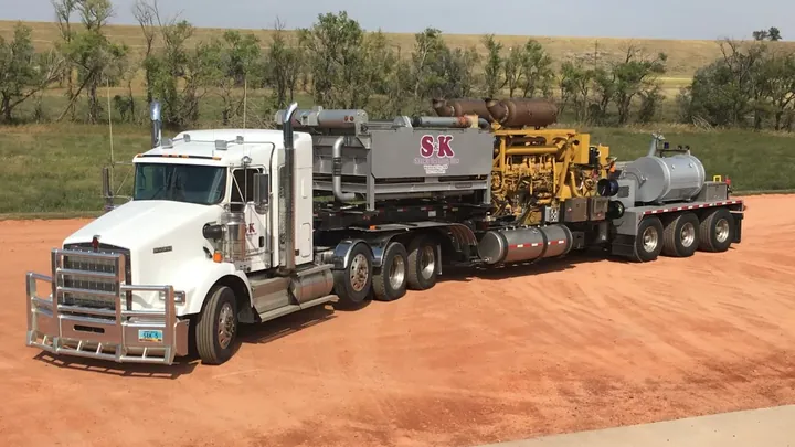 An S&K Kenworth hauling a pump unit on a red scoria pad