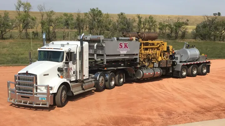 An S&K Kenworth hauling a pump unit on a red scoria pad