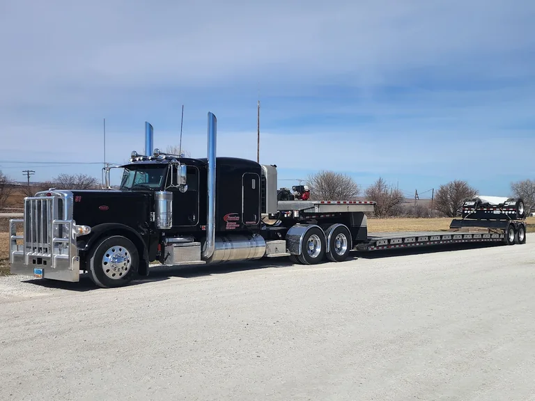 A black StateLine truck hooked to a lowboy trailer