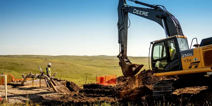 A TTK excavator digging, with a hand working the ditch beside it