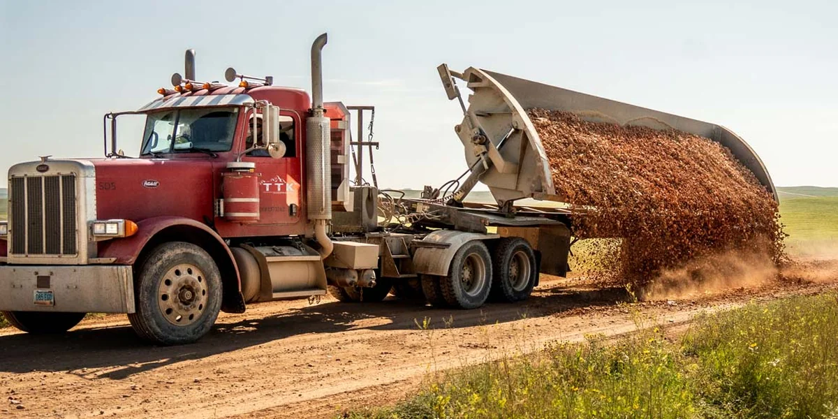 A TTK side dump truck dumping gravel on a dirt road
